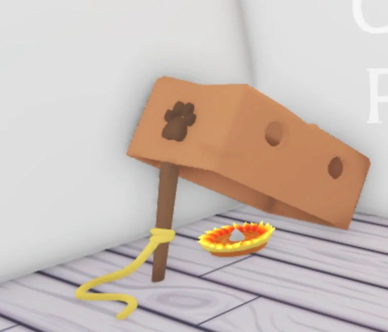 A Box Lure placed in an Adopt Me house, a cardboard box propped up on a stick with a rope